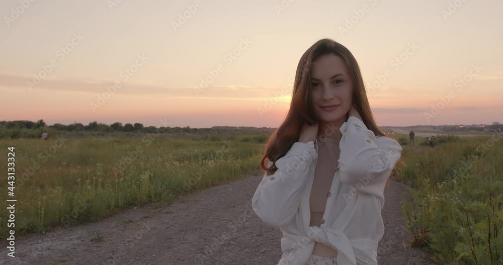 Tender caucasian woman with wavy brown hair posing during amazing sunset among wild field. Beautiful nature at countryside. Carefree concept. Tender caucasian woman with wavy brown hair posing during amazing sunset among wild field. Beautiful nature at countryside. Carefree concept.