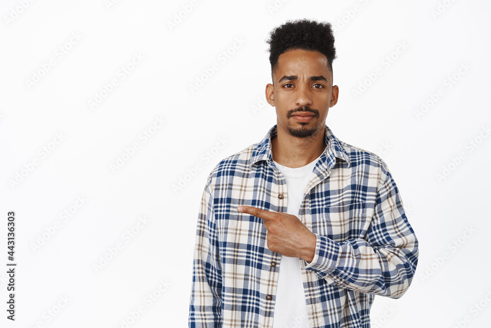 Sad african american guy, young man pointing finger left, frowning and looking let down, upset and disappointed about smth, showing bad promo text, white background Sad african american guy, young man pointing finger left, frowning and looking let down, upset and disappointed about smth, showing bad promo text, white background