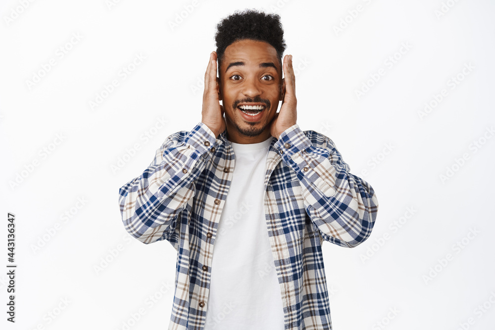 Face expression. Happy and excited african american man look amazed, smiling, holding hands near face and staring thrilled at camera, hear awesome news, white background Face expression. Happy and excited african american man look amazed, smiling, holding hands near face and staring thrilled at camera, hear awesome news, white background