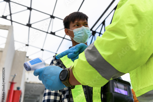 Labour Screening, Construction foreman wearing protective face mask pointing measurement results of body temperature of welder worker in an Infrared Thermometer during coronavirus COVID-19 Pandemic