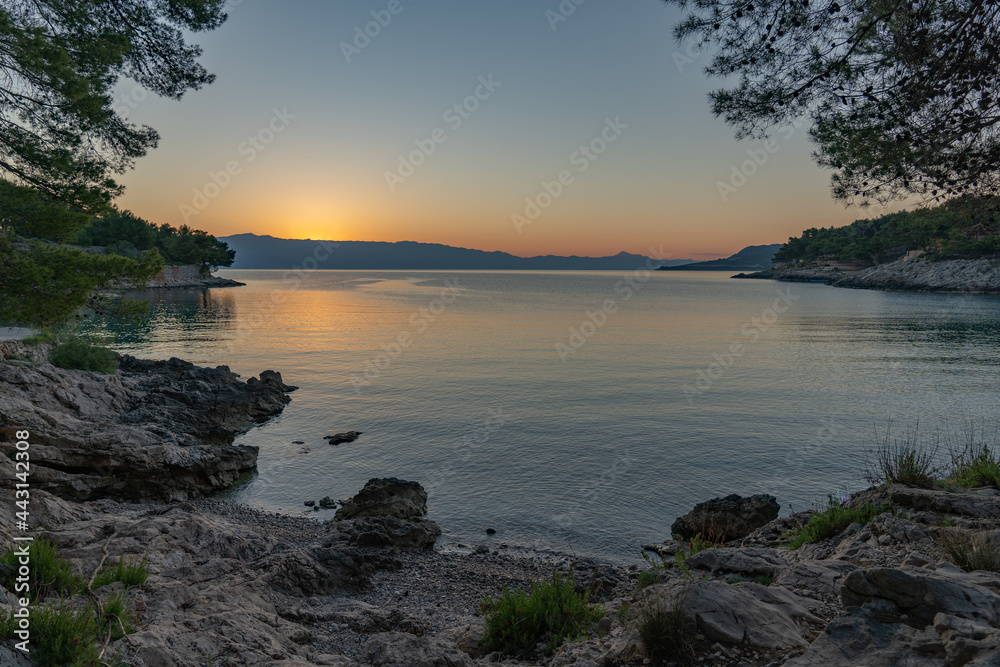The sun just above the sea horizon creating a sunrise / sunset with a panorama of the mountains and rocky beaches