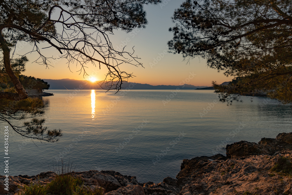 The sun just above the sea horizon creating a sunrise / sunset with a panorama of the mountains and rocky beaches The sun just above the sea horizon creating a sunrise / sunset with a panorama of the mountains and rocky beaches
