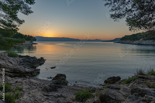 The sun just above the sea horizon creating a sunrise / sunset with a panorama of the mountains and rocky beaches © Tomasz