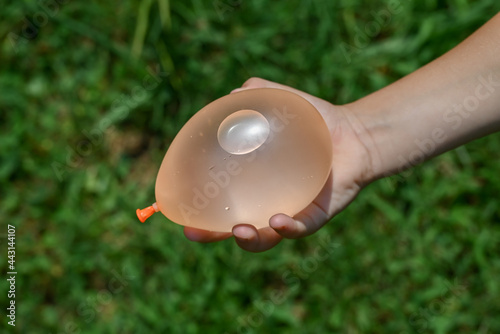Child's hand holding orange water balloon