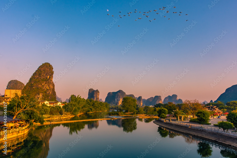 Fototapeta premium Flock of birds flying over the Li River in Yangshuo at sunset, China