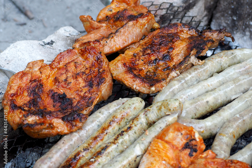 marinated chicken meat and sausages are cooked in nature on a metal barbecue net . side view marinated chicken meat and sausages are cooked in nature on a metal barbecue net . side view