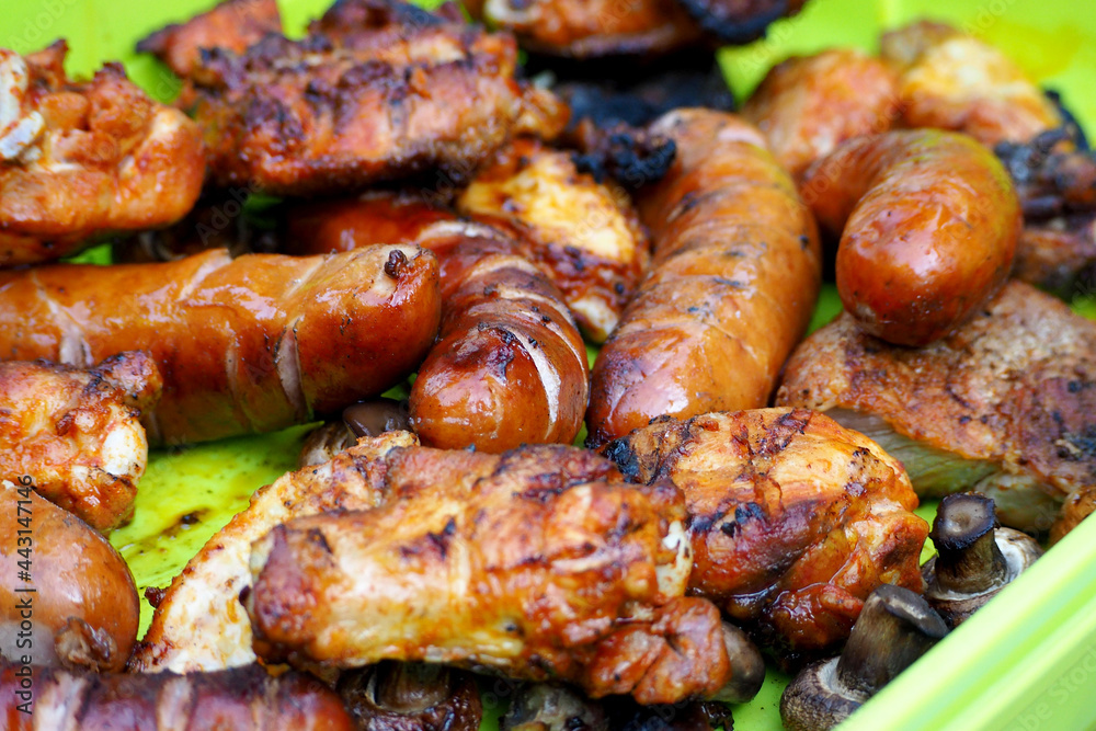 sausages, chicken wings and legs after the grill lies on a green plate . side view