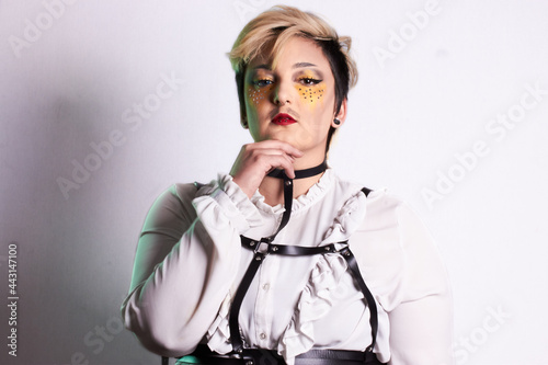 Drag King James Capone in a white frilly shirt and leather chest harness on a plain backdrop photo