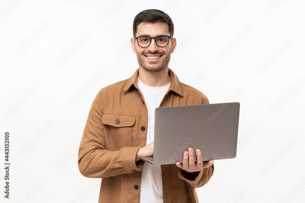 Studio portrait of young man standing holding laptop and looking at camera with happy smile, isolated on gray Studio portrait of young man standing holding laptop and looking at camera with happy smile, isolated on gray