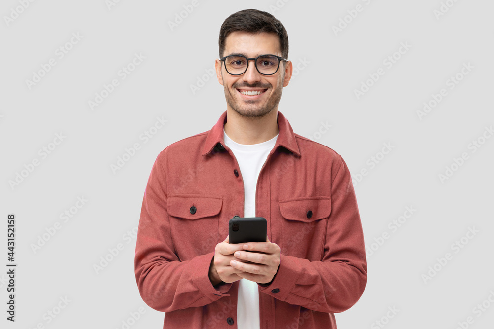 Young modern man holding smart phone in hands, looking at camera with smile, isolated on gray background Young modern man holding smart phone in hands, looking at camera with smile, isolated on gray background