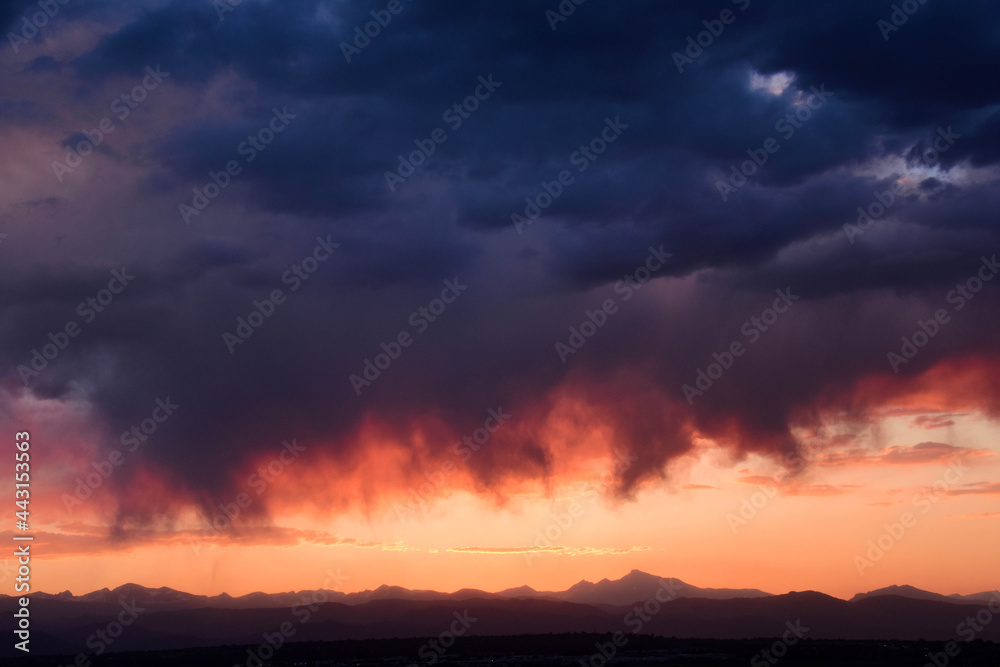 dramatic virga clouds at sunset over the front range of the colorado rocky mountains, as seen from broomfield, colorado 