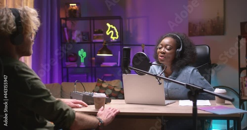 Waist up portrait view of the two diverse people talking and recording audio podcast at the table at radio station while working together. Broadcasting concept photo