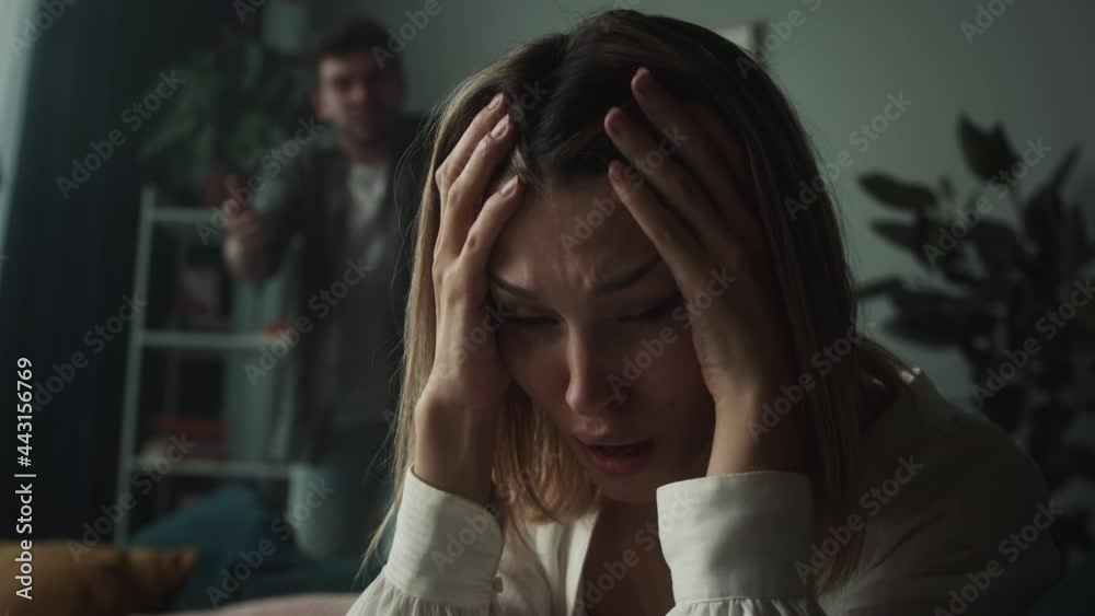 Irritated emotional man shouting at woman in living room at home, husband screaming at his wife holding her head, feeling anger and stress, bad mood. Scandals and quarrels in family.