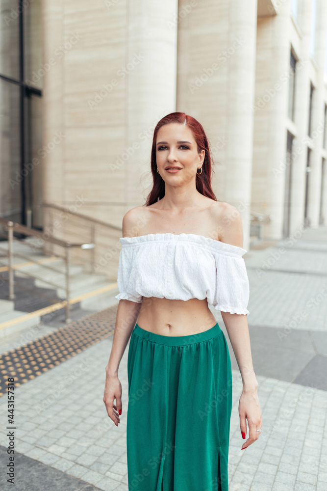 Redheaded woman in summer clothes in front of a building posing for the camera Redheaded woman in summer clothes in front of a building posing for the camera