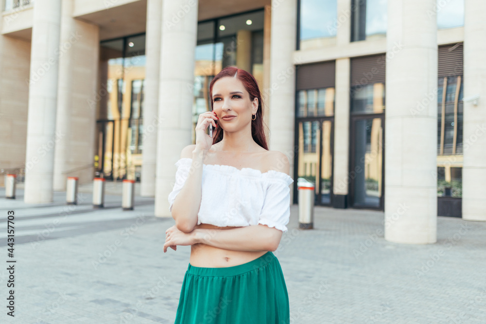 Redheaded girl talking on her smartphone in the city in summer