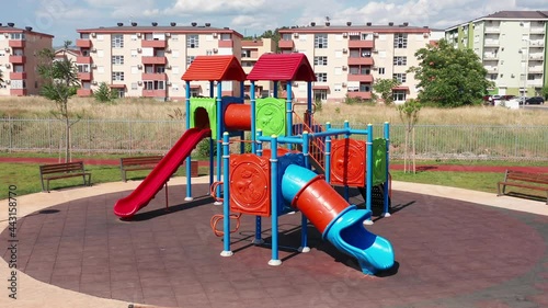 Empty playhouse and slide in a playground for kids. Deserted kindergarten park for children in residential neighborhood of a city. Colorful equipment with apartment condo buildings in background.