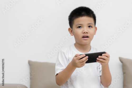 Happy little boy having fun playing game on mobile phone, Preschool kid sitting on sofa with smiling face watching cartoon on smartphone, Child using cell phone while relaxing at home © Keopaserth
