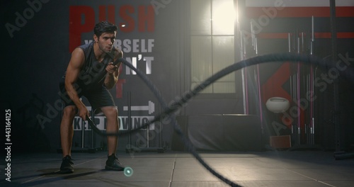 Muscular athletic Caucasian young man strong effort with battle rope waves doing exercise while working out in fitness gym, Cross fit training, People power sport health lifestyle concept