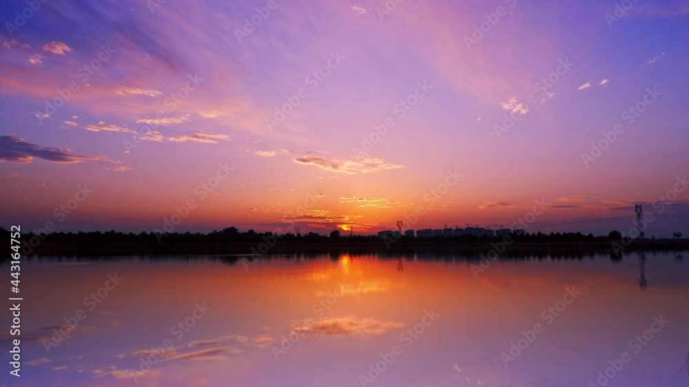 Time-lapse of lake at sunset, clouds in purple sky with reflection on water
