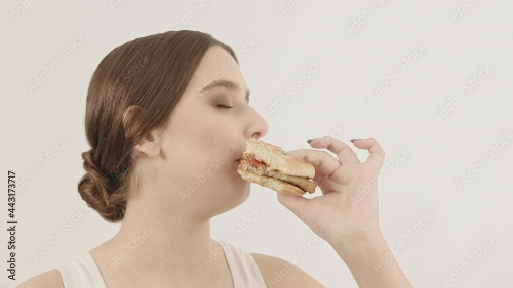 The girl holds a burger and eats it. Fast intake of junk food. The girl holds a burger and eats it. Fast intake of junk food.