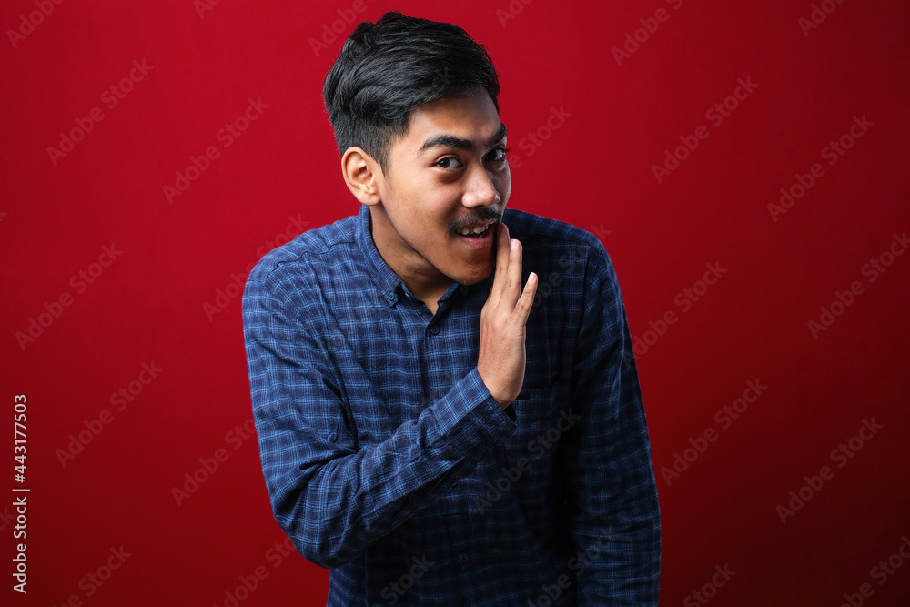 Young handsome man with beard wearing casual shirt hand on mouth telling secret rumor, whispering malicious talk conversation Young handsome man with beard wearing casual shirt hand on mouth telling secret rumor, whispering malicious talk conversation