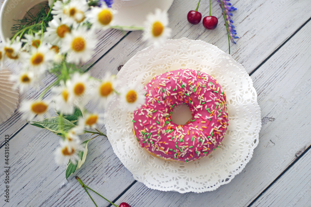 Donut in pink glaze on a background of wild flowers of chamomiles, fresh berries on a wooden table Donut in pink glaze on a background of wild flowers of chamomiles, fresh berries on a wooden table