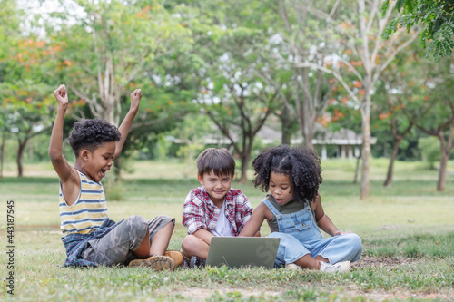 Groups of ethnic children sitting on the lawn and having fun using computers together.African American curly hair,positive emotion