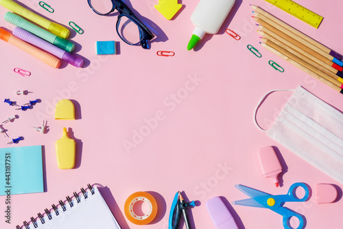 Back to school bright concept, frame with colorful school supplies with medical mask on pink background .