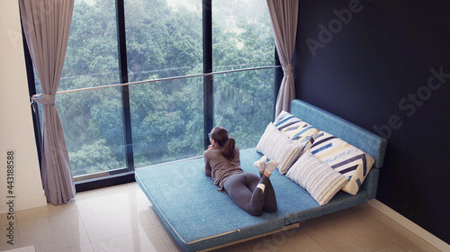 Asian business woman in casual wear relaxing on sofa in holiday time at living room, Summer holiday vacation travel trip, rain outside the window. photo