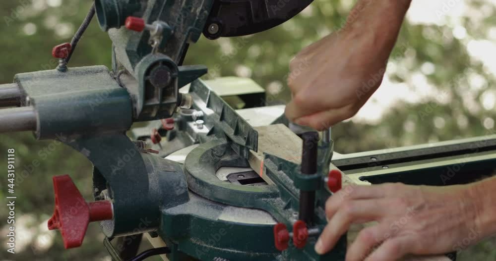 Carpenter fixing wood plank and making slow cross cut on wood plank using miter saw, close-up Carpenter fixing wood plank and making slow cross cut on wood plank using miter saw, close-up