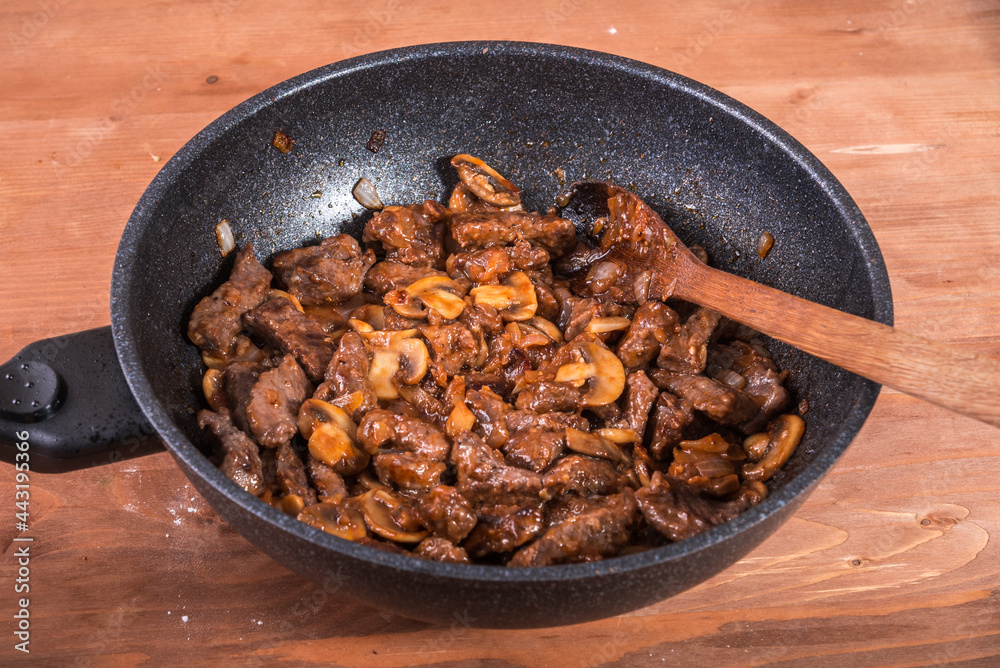 Fototapeta premium Cooking beef stroganoff with mushrooms - fried cuts of beef with mushrooms in a pan, close-up
