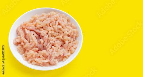 Minced meat of chicken fillet in white plate on yellow background.