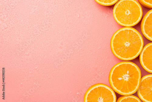 Top view photo of cut oranges and drops on isolated pastel pink background with copyspace on the left