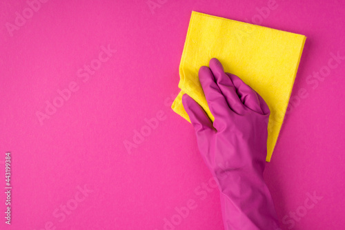 Top view photo of hand in pink glove using yellow rag on isolated pink background with copyspace