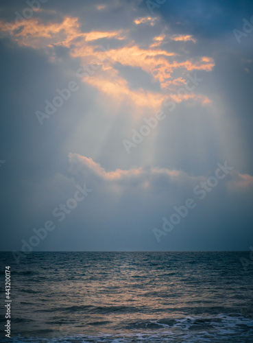 Beautiful sun shines through the clouds above the sea after a storm in the evening.