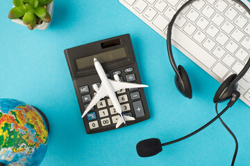Top view photo of black headset with microphone on white keyboard plant globe and plane model on calculator in the middle on isolated pastel blue background