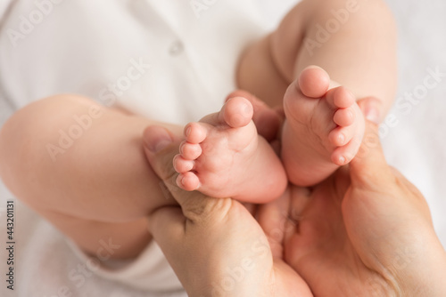 Closeup photo of mother's hands holding baby's tiny feet on isolated white cloth background