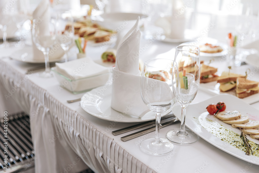 Fototapeta premium Table setting for a banquet or celebration. Empty wine glasses for spirits, champagne and juice. Set the table. Cloth napkins on a platter. Banqueting hall. Cold appetizers and salads