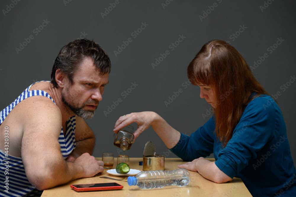 Photo angry man and woman are sitting at the table and pours alcohol into a glass Photo angry man and woman are sitting at the table and pours alcohol into a glass