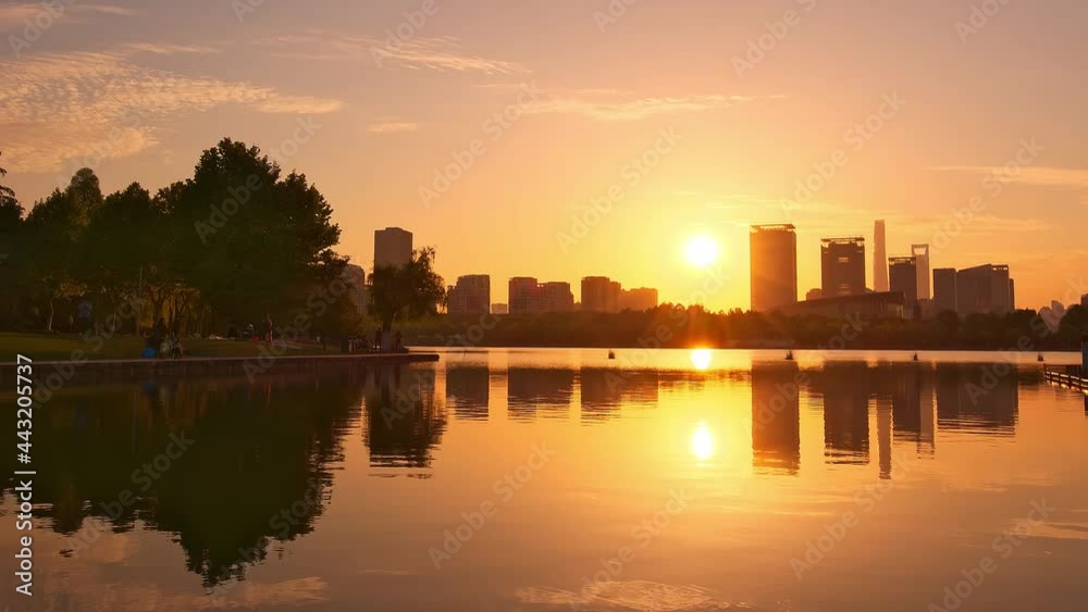 Time-lapse of lake in city park at sunset, reflection of sun and buildings by lake on water Time-lapse of lake in city park at sunset, reflection of sun and buildings by lake on water
