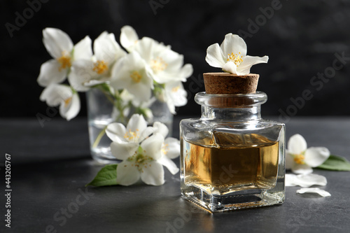 Jasmine essential oil and fresh flowers on dark grey table, space for text
