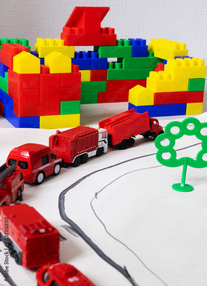 Fototapeta premium A toy car fire brigade drives along a painted road past a house made of plastic bricks. Copy space