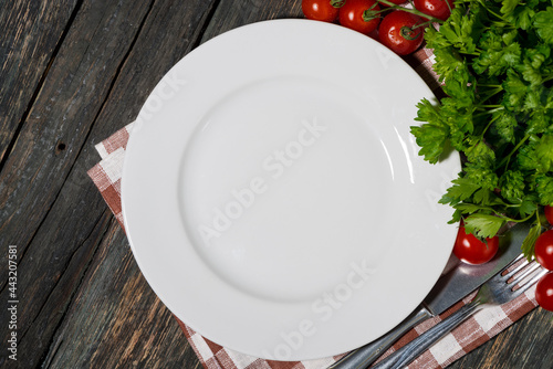 table setting with white plate and vegetables on wooden background, top view
