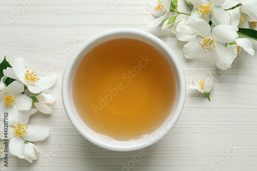Aromatic jasmine tea and fresh flowers on white wooden table, flat lay