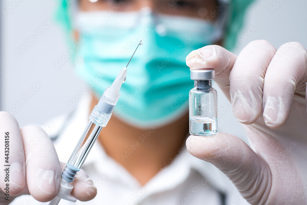 Doctor wears face mask and white medical glove hand holding flu, covid-19 liquid vaccine vial bottle and syringe are filling for preparing injection. Vaccination for fight Covid-19 virus concept. Doctor wears face mask and white medical glove hand holding flu, covid-19 liquid vaccine vial bottle and syringe are filling for preparing injection. Vaccination for fight Covid-19 virus concept.