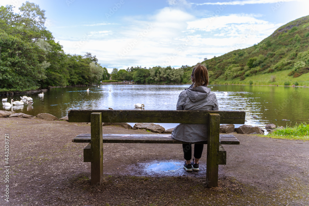 young lonely woman seated on a bench near a lake
