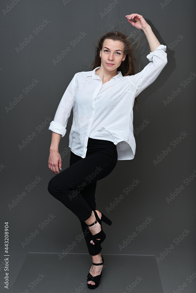 Full-length portrait of a caucasian girl posing on a gray background in a white shirt and black trousers