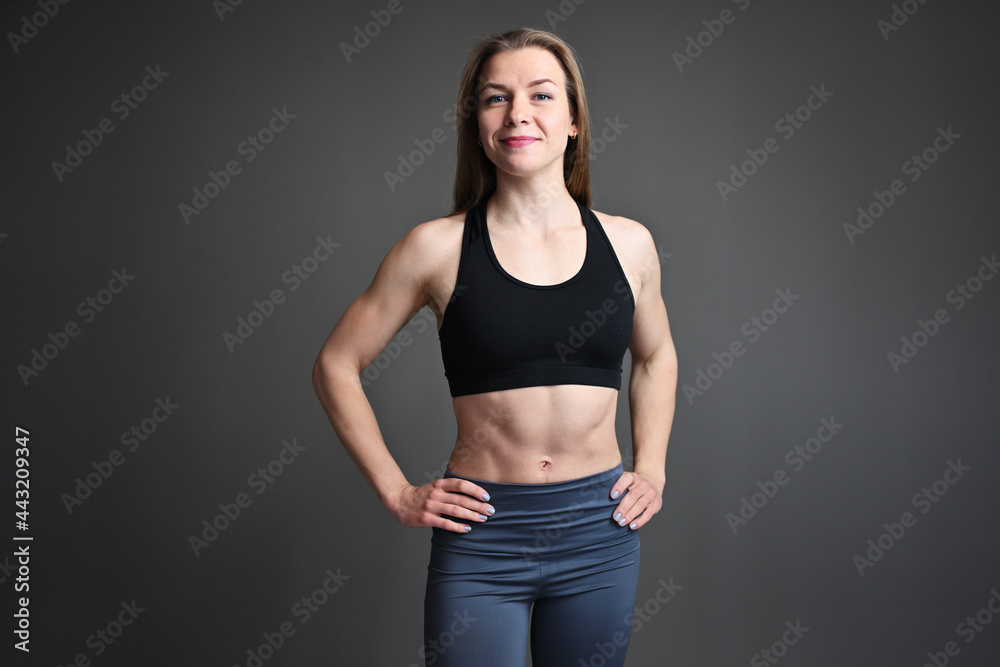 Caucasian fitness girl standing straight with a smile on a gray background. Looking at camera Caucasian fitness girl standing straight with a smile on a gray background. Looking at camera
