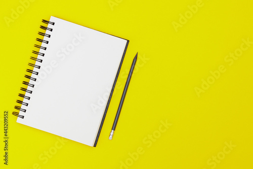 Blank spiral notebook and pencil on yellow background. Top view with copy space for input the text.