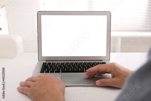 Man with modern laptop at white table indoors, closeup. Space for design